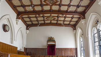 Maison Dieu Dover Court Room. On the left is a round time piece. In the centre is a red furnished chair. On the left are two arched windows.